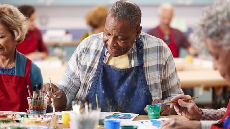 A senior painting with a brush during a class