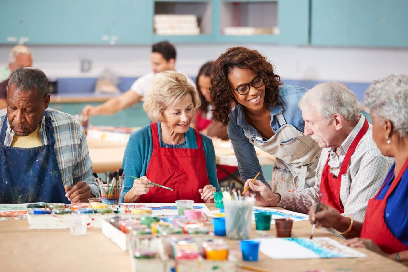 Seniors painting together around a studio table with a smiling instructor