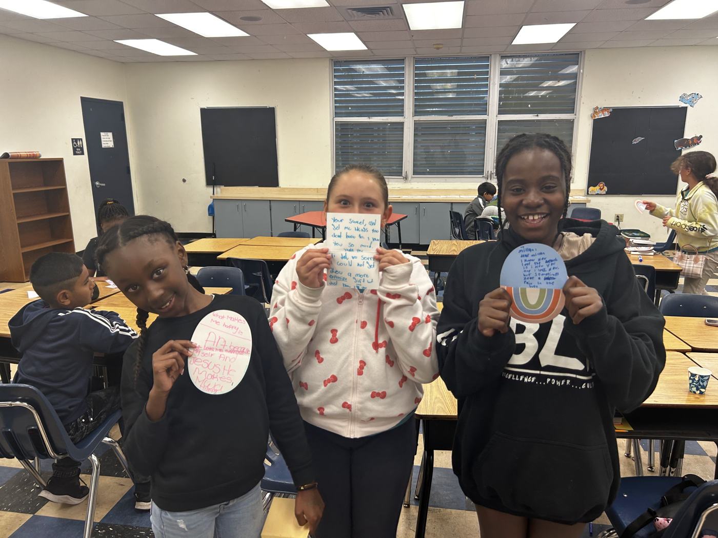 Three students holding up their finished paper plate art